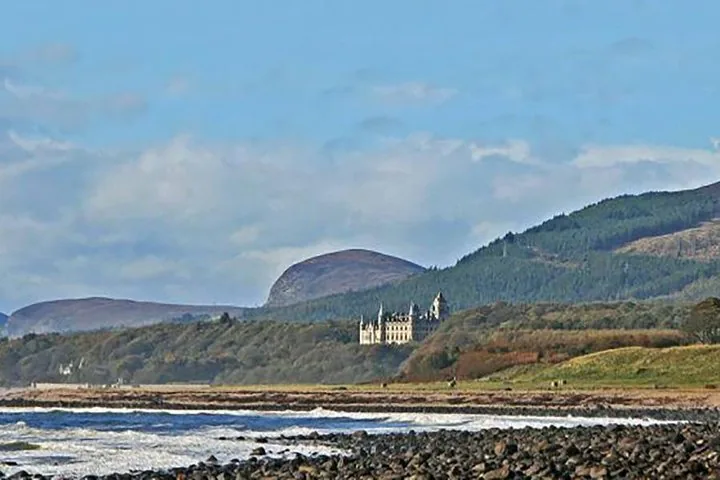 Fernblick auf Dunrobin Castle, eingebettet an einen Hang, von einer felsigen Küste aus gesehen.