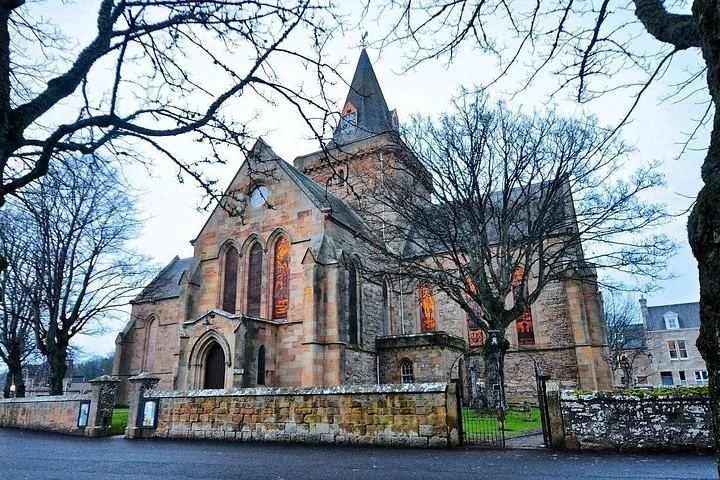 Ein Kirchengebäude aus Stein mit Buntglasfenstern und einem hohen Kirchturm an einem bewölkten Tag.