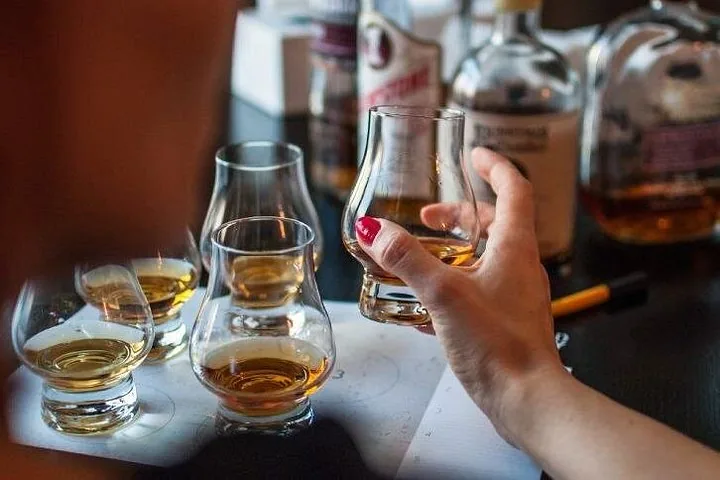 Eine Person hält während einer Verkostung ein Glas Whisky; weitere Gläser stehen auf dem Tisch.