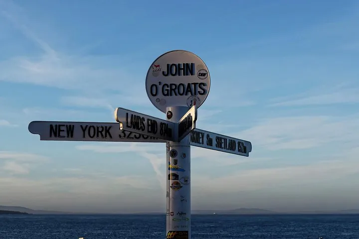 Iconic John O'Groats signpost pointing to various distant locations against a blue sky.